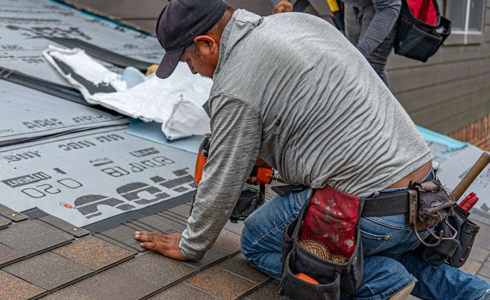 A roofer installing shingles on a house roof